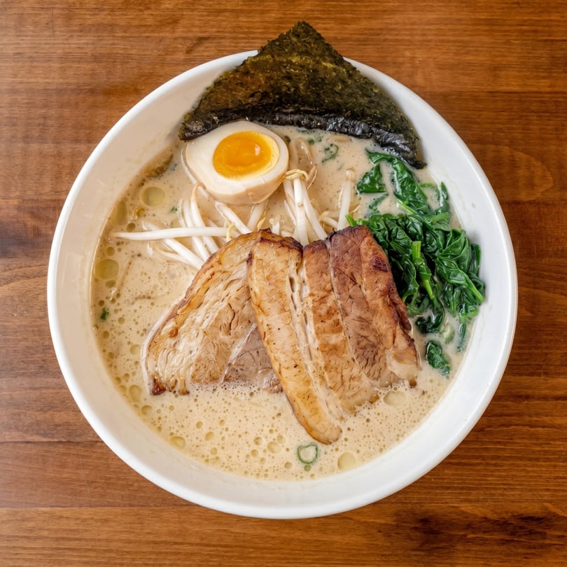 A bowl of creamy ramen with pork belly, a soft-boiled egg, bean sprouts, spinach, and nori.