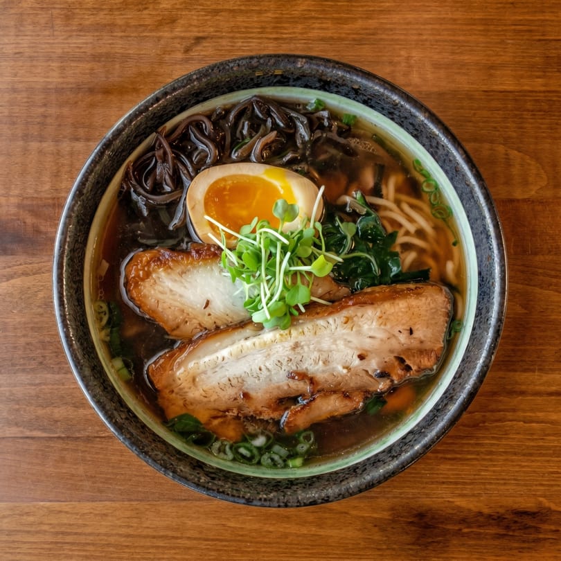 Overhead view of a ramen bowl with pork belly, soft-boiled egg, noodles, and microgreens.